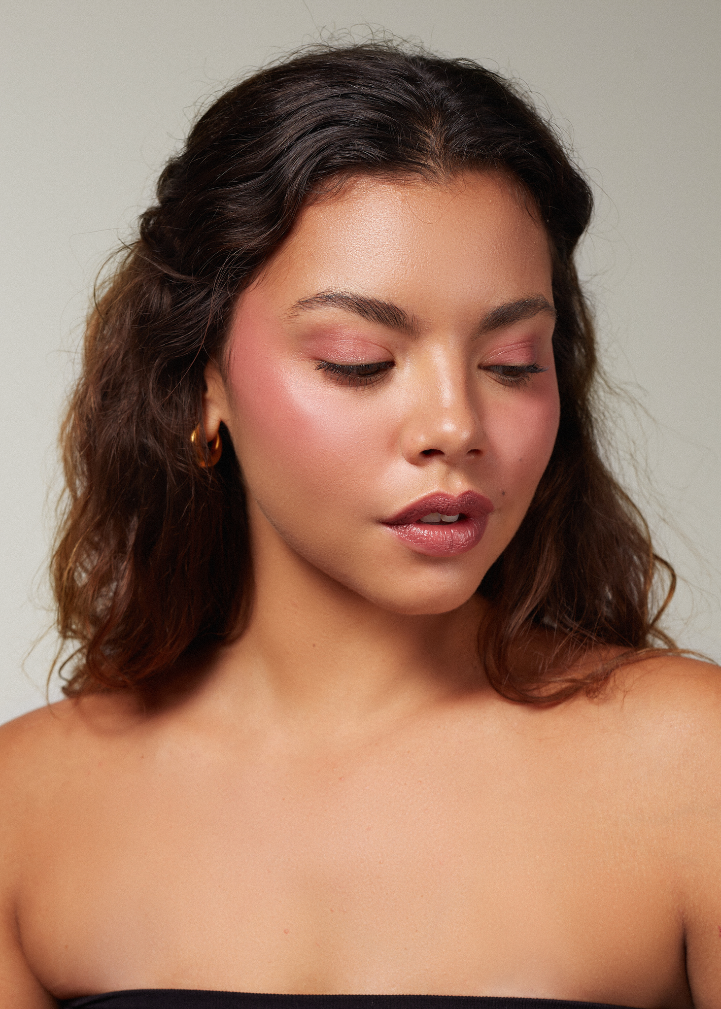 beautiful brunette woman with glowy skin and rosy cheeks looking down, wearing Canggu balm. 