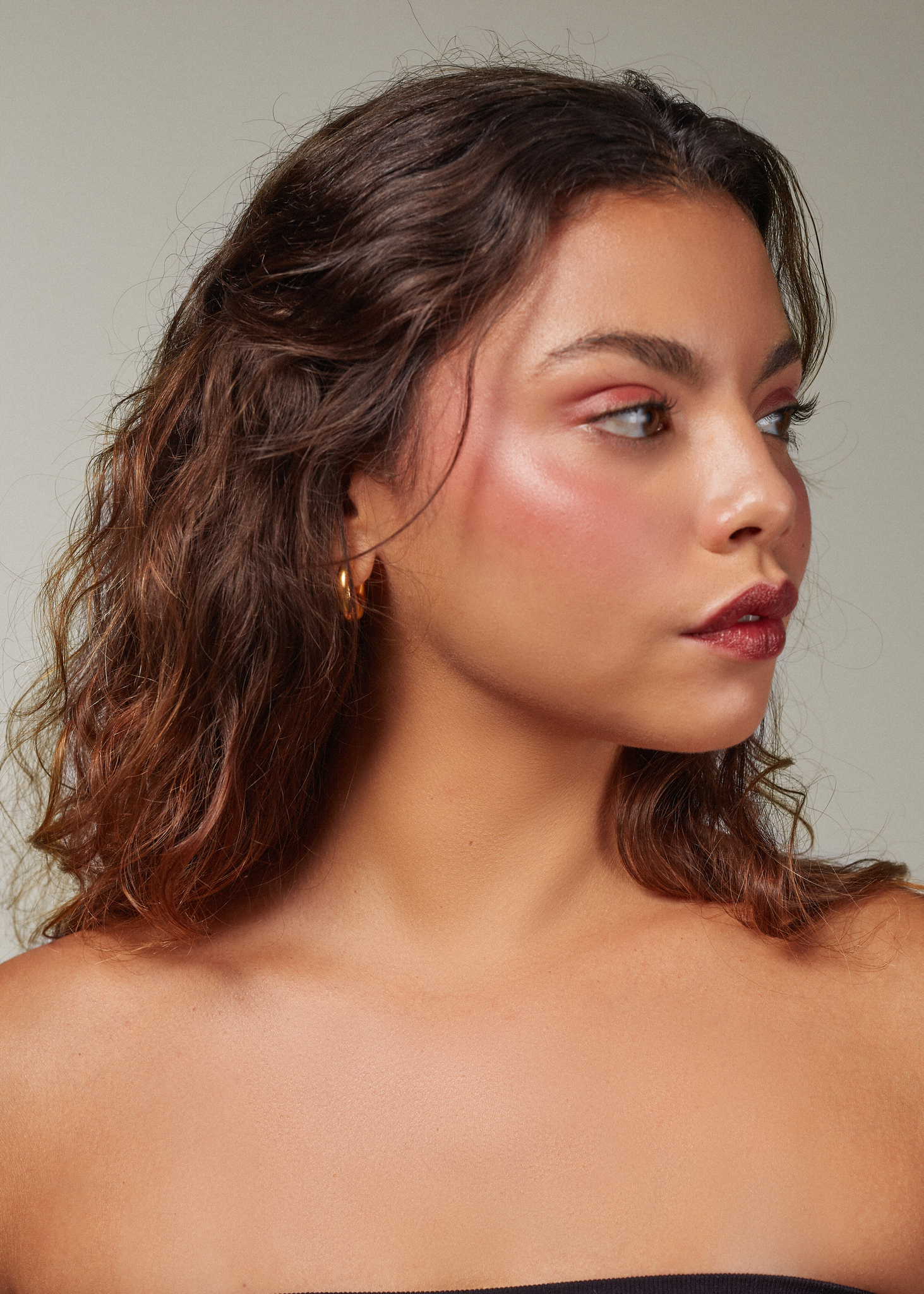 Portrait of a brunette woman with glowy, beautiful skin and rosy cheeks looking to her side.